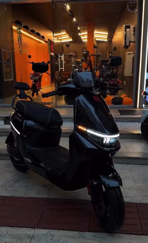 Scooter preta na calçada em frente à vitrine iluminada da loja Wave à noite